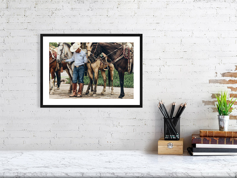 Colour photograph of horses and rider at rest displayed as a small framed print in a styled interior desktop setting (mockup)
