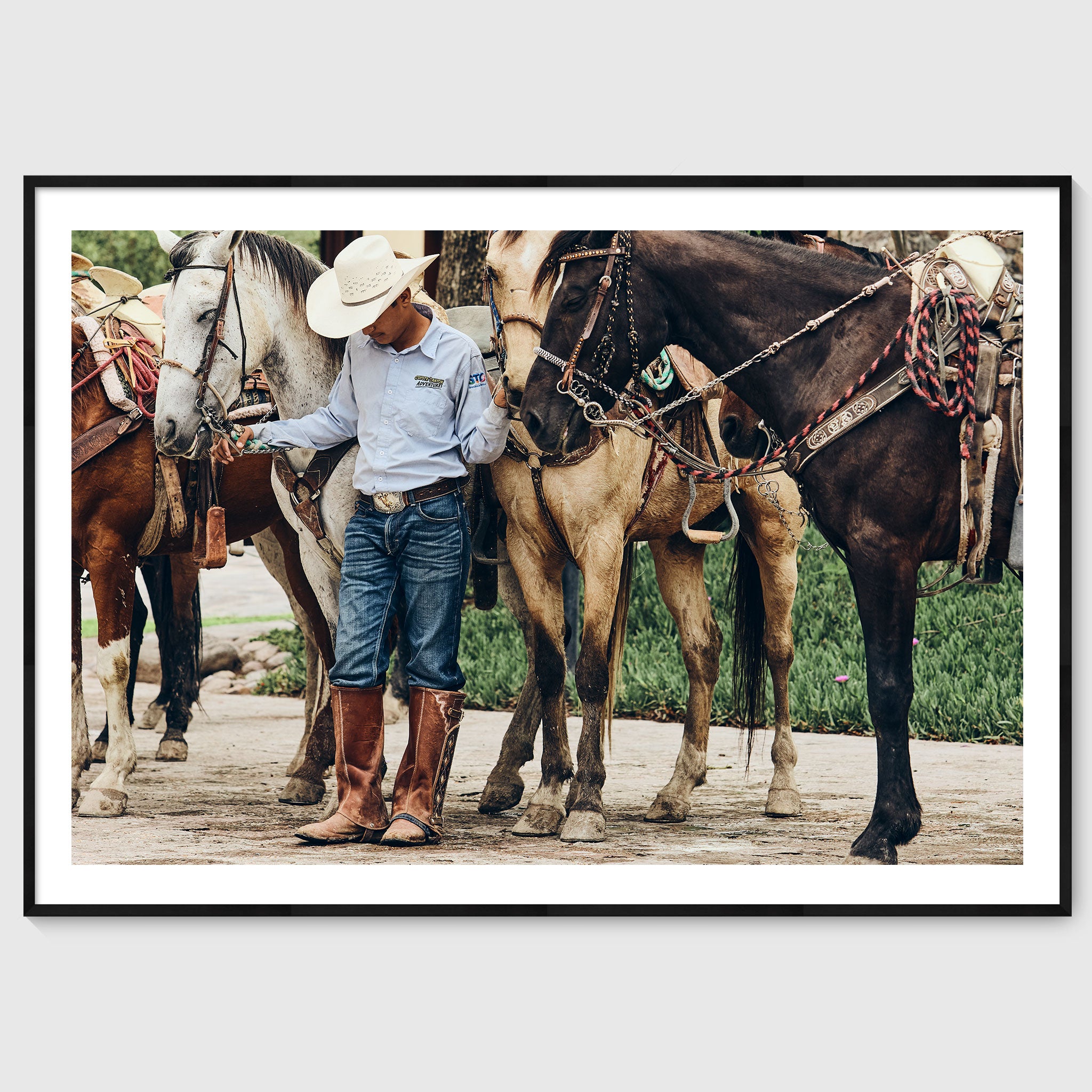 Colour photograph of a young horseman standing quietly among saddled horses during a traditional gathering in San Miguel de Allende, shown in a black wooden frame