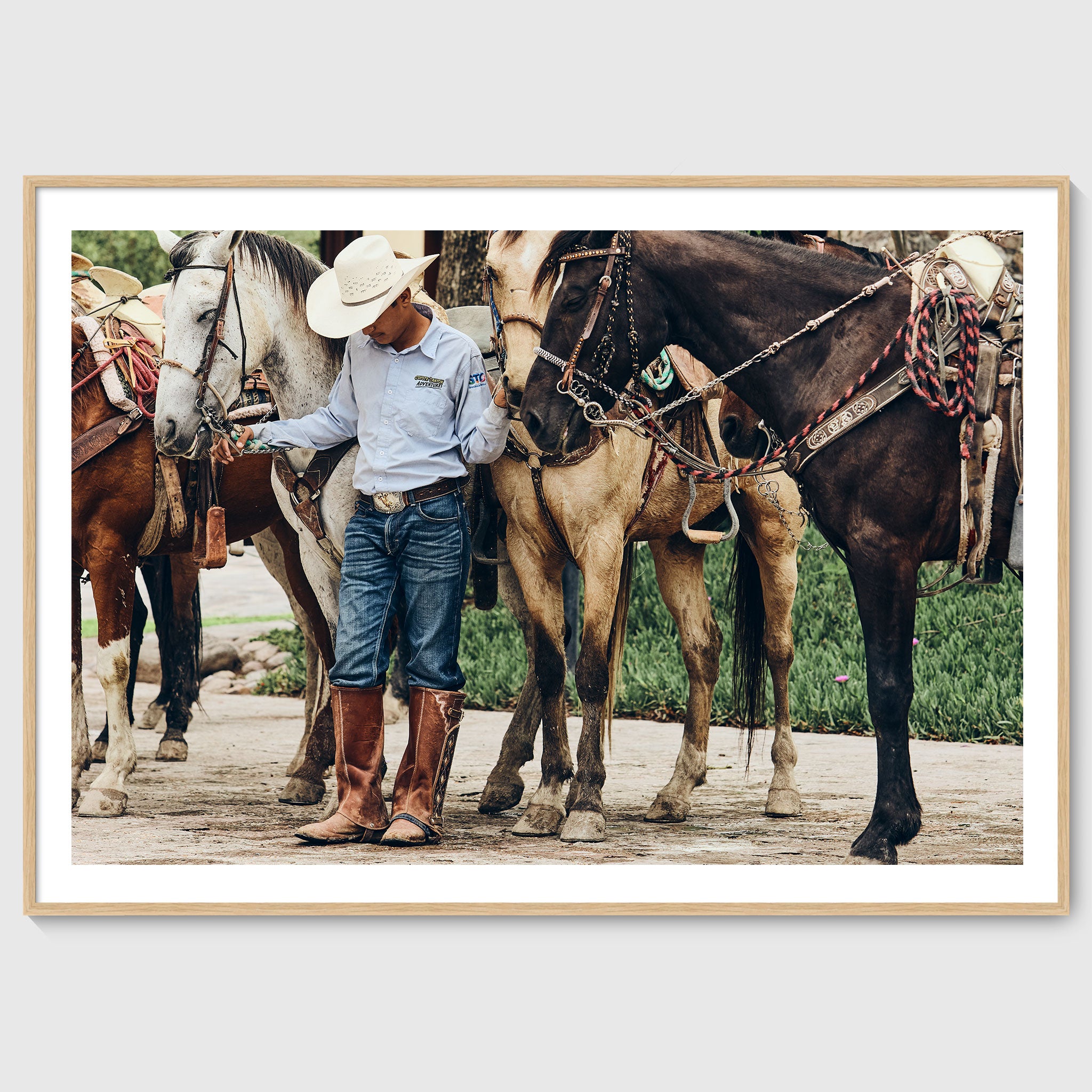 Colour photograph of a young horseman standing quietly among saddled horses during a traditional gathering in San Miguel de Allende, shown in an oak wooden frame