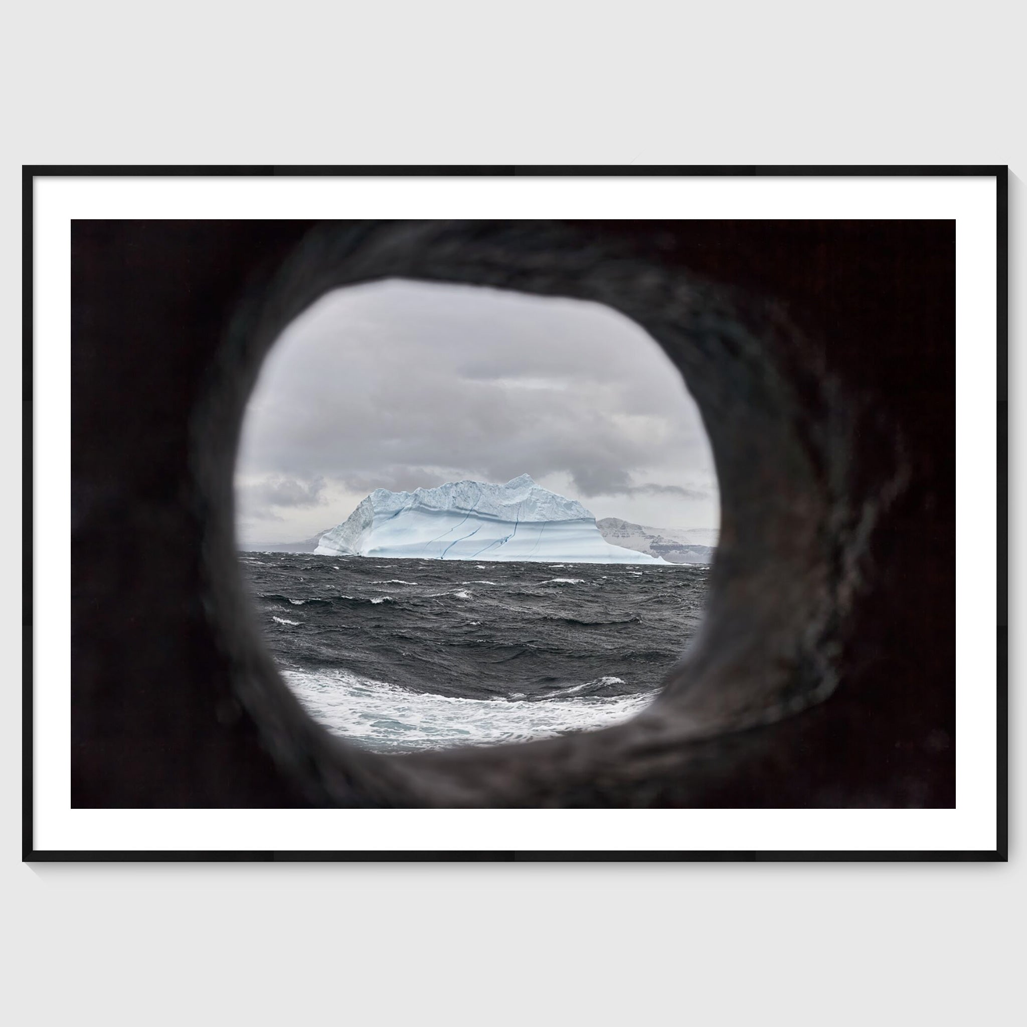 Colour photograph of an iceberg viewed through a ship’s scupper, shown in a black frame, Greenland