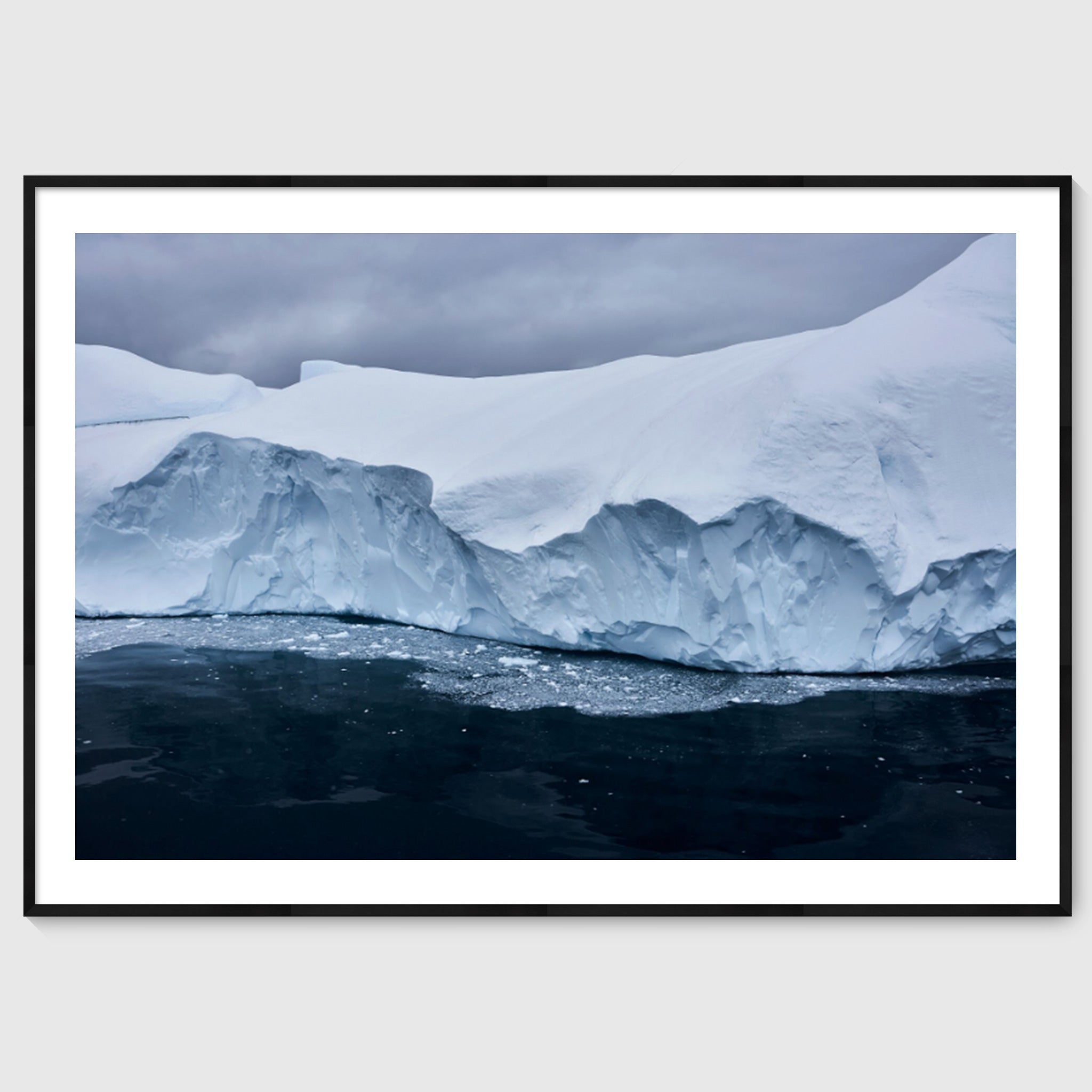 Colour photograph of a glacier edge with fractured ice and dark water below, shown in a black frame, Greenland