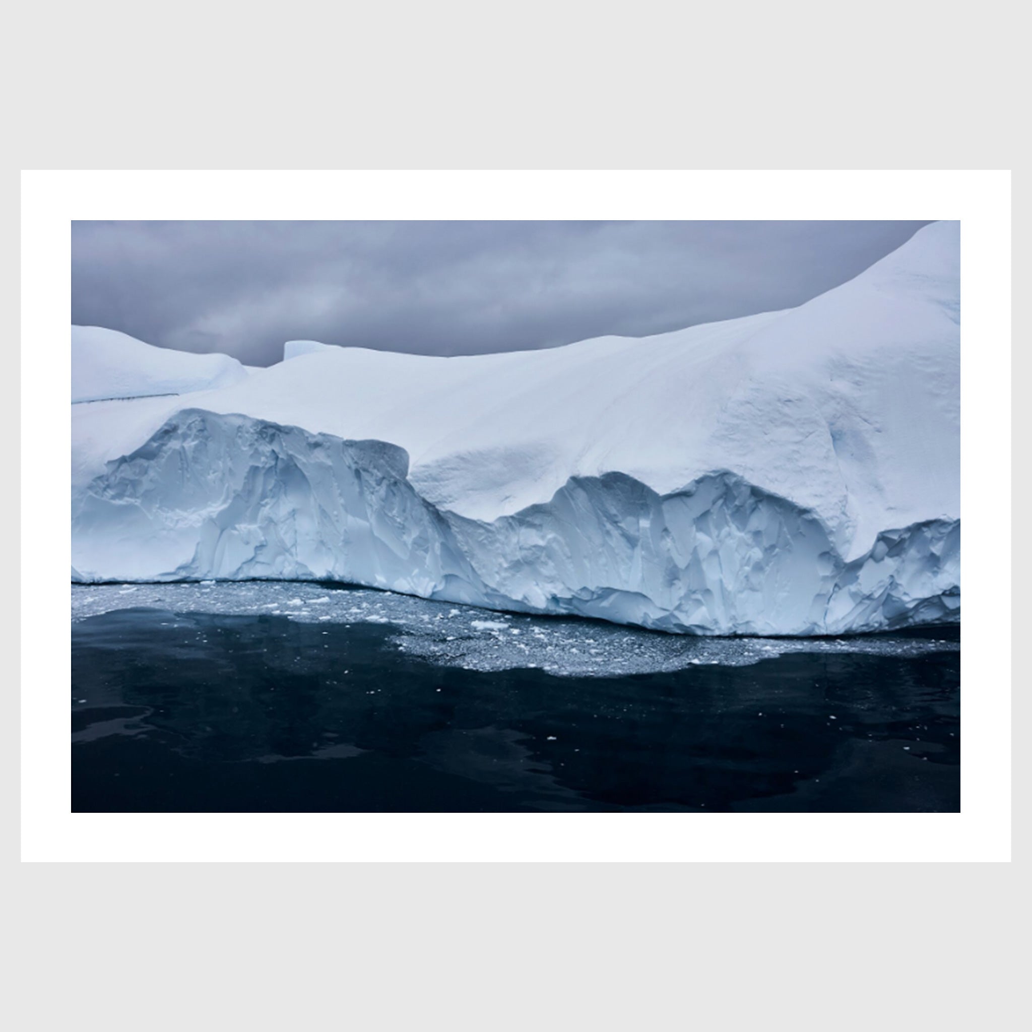 Colour photograph of a glacier edge with fractured ice and dark water below, Greenland