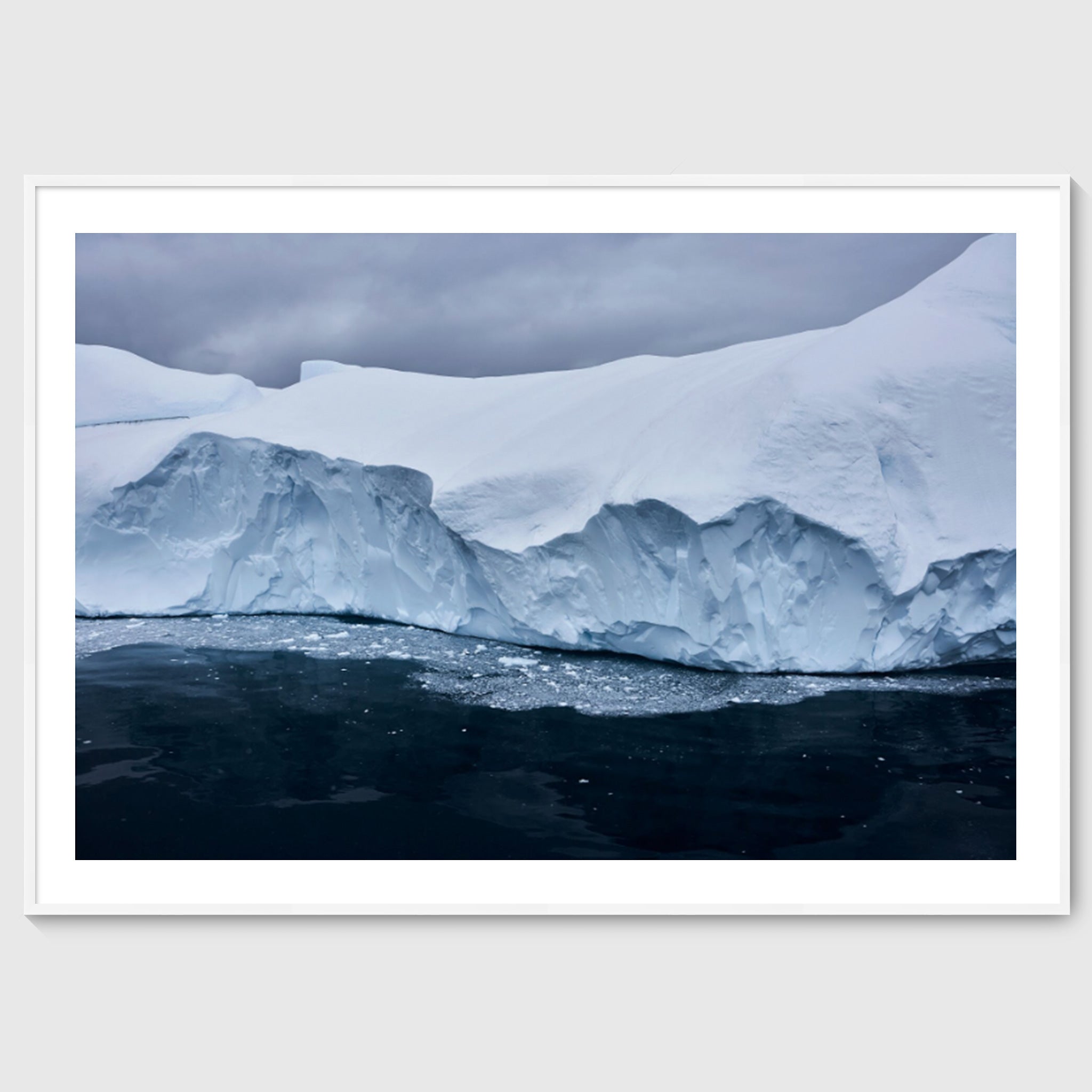Colour photograph of a glacier edge with fractured ice and dark water below, shown in a white frame, Greenland