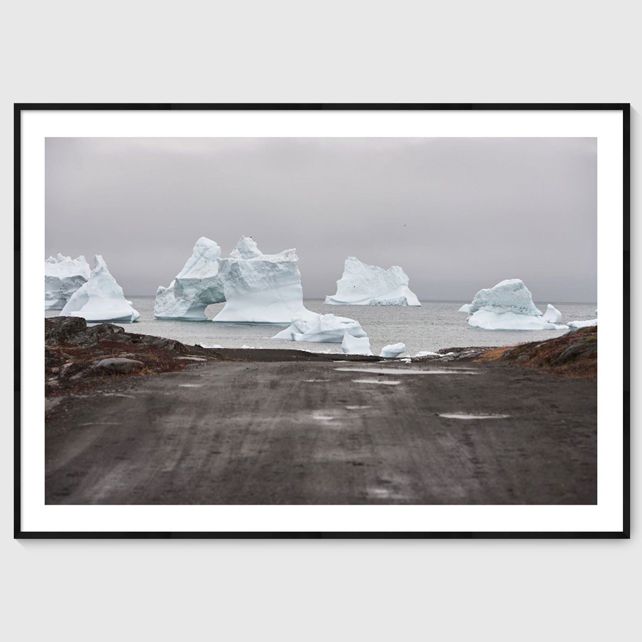 Colour photograph of icebergs at the end of a gravel road leading to the sea, shown in a black frame, Greenland