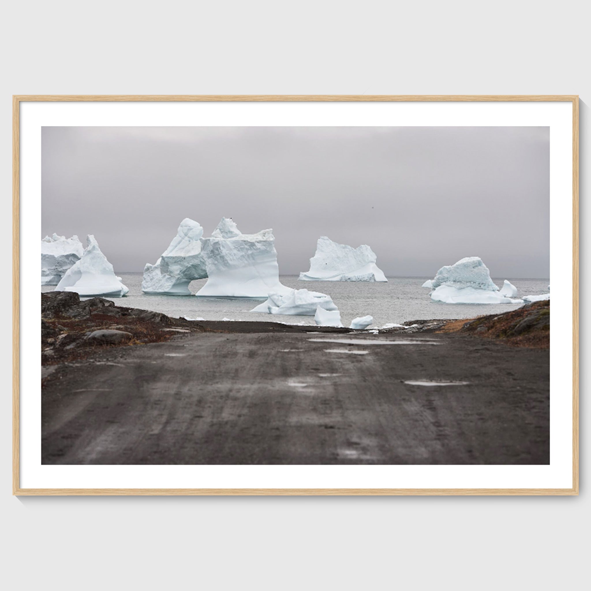 Colour photograph of icebergs at the end of a gravel road leading to the sea, shown in an oak frame, Greenland
