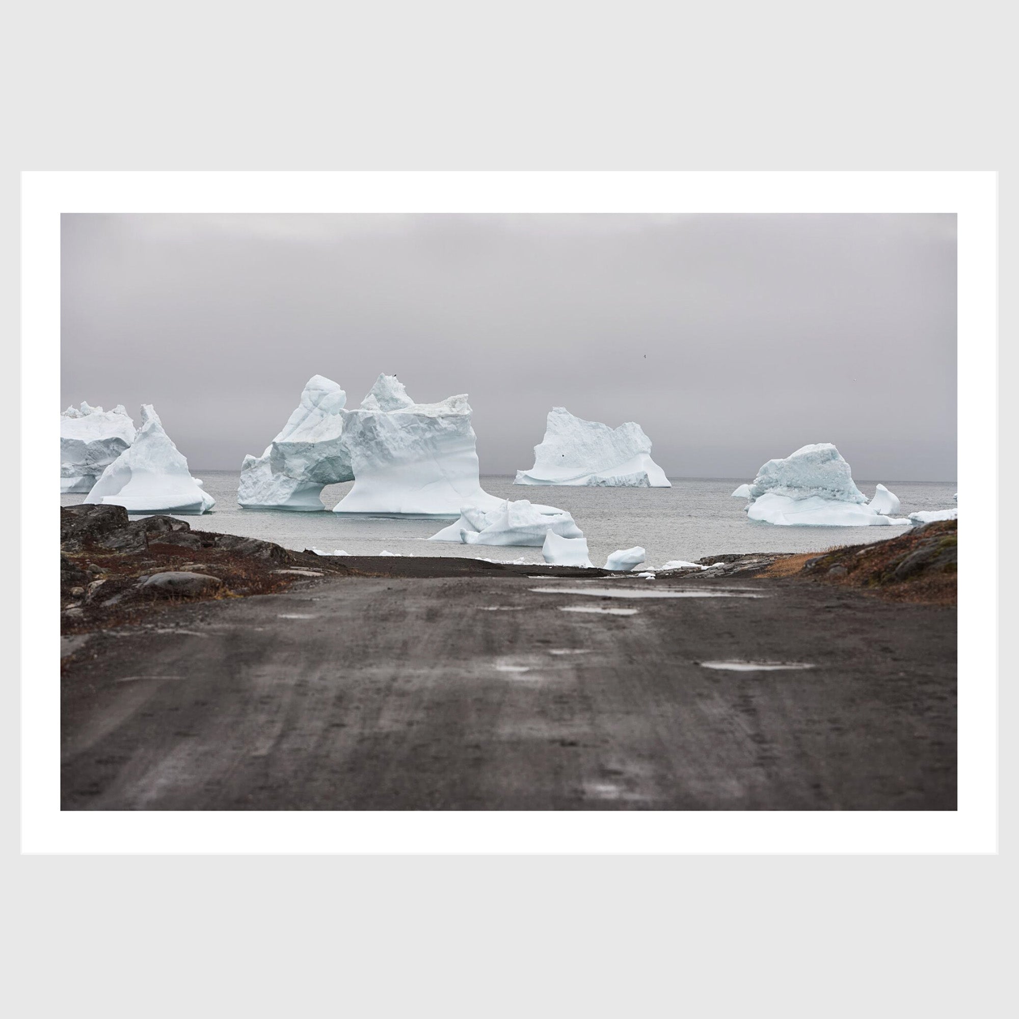 Colour photograph of icebergs at the end of a gravel road leading to the sea, Greenland