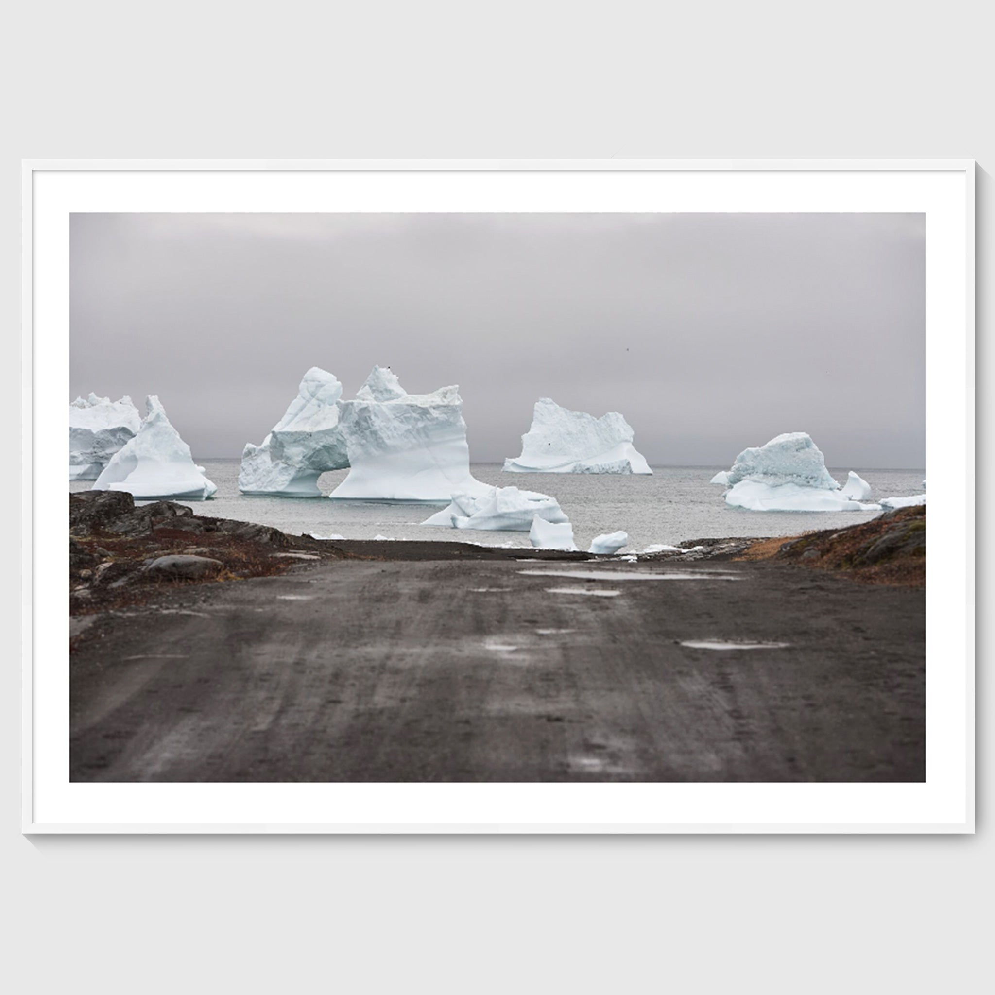 Colour photograph of icebergs at the end of a gravel road leading to the sea, shown in a white frame, Greenland