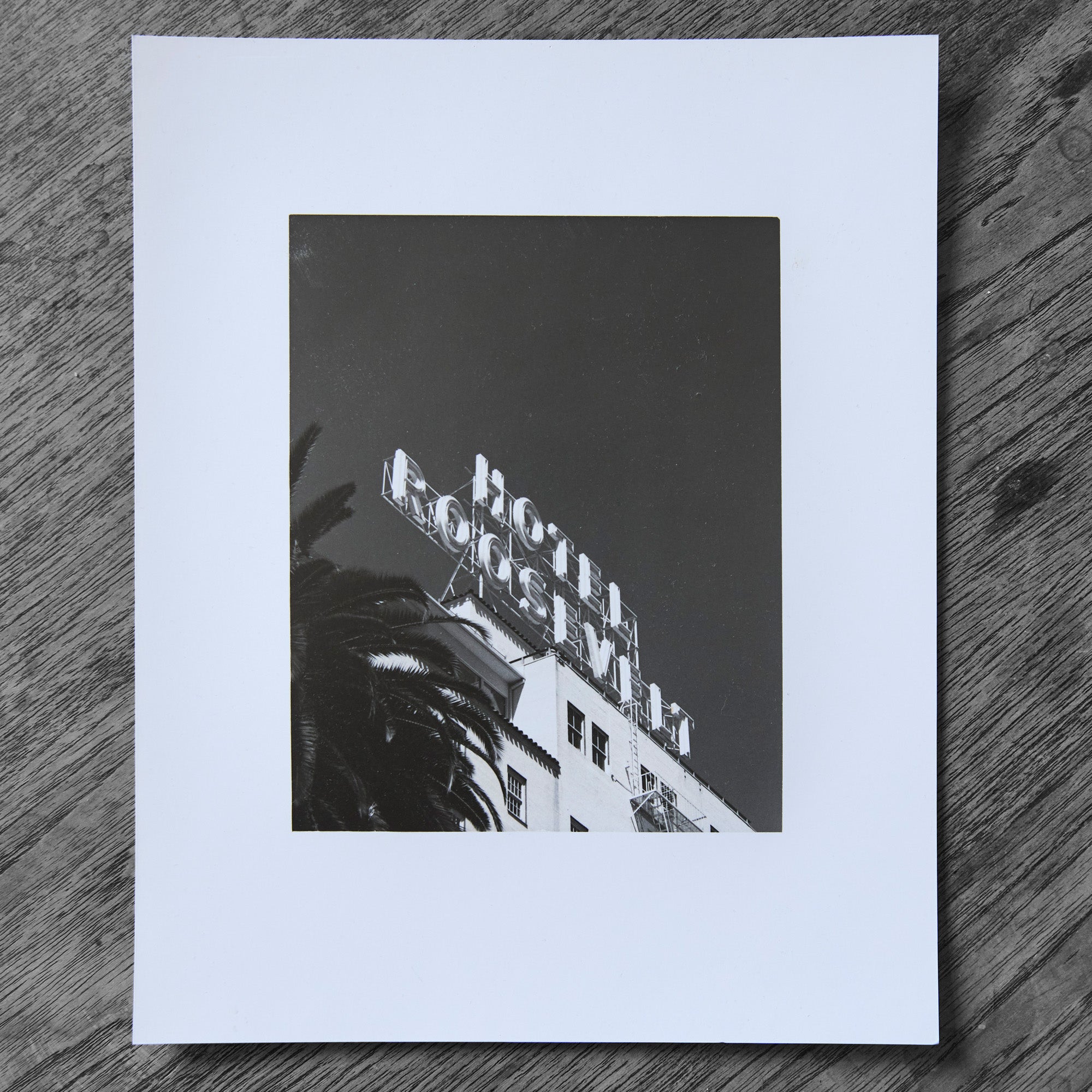 One-off black and white darkroom photograph of a hotel rooftop sign and palm tree against a cloudless sky, hand-printed by the artist.