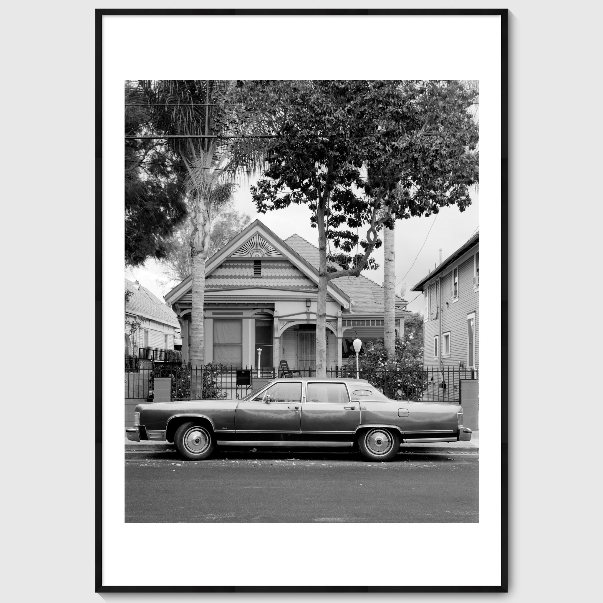 Black and white photograph of a parked car in front of a suburban house, shown in a black frame, California