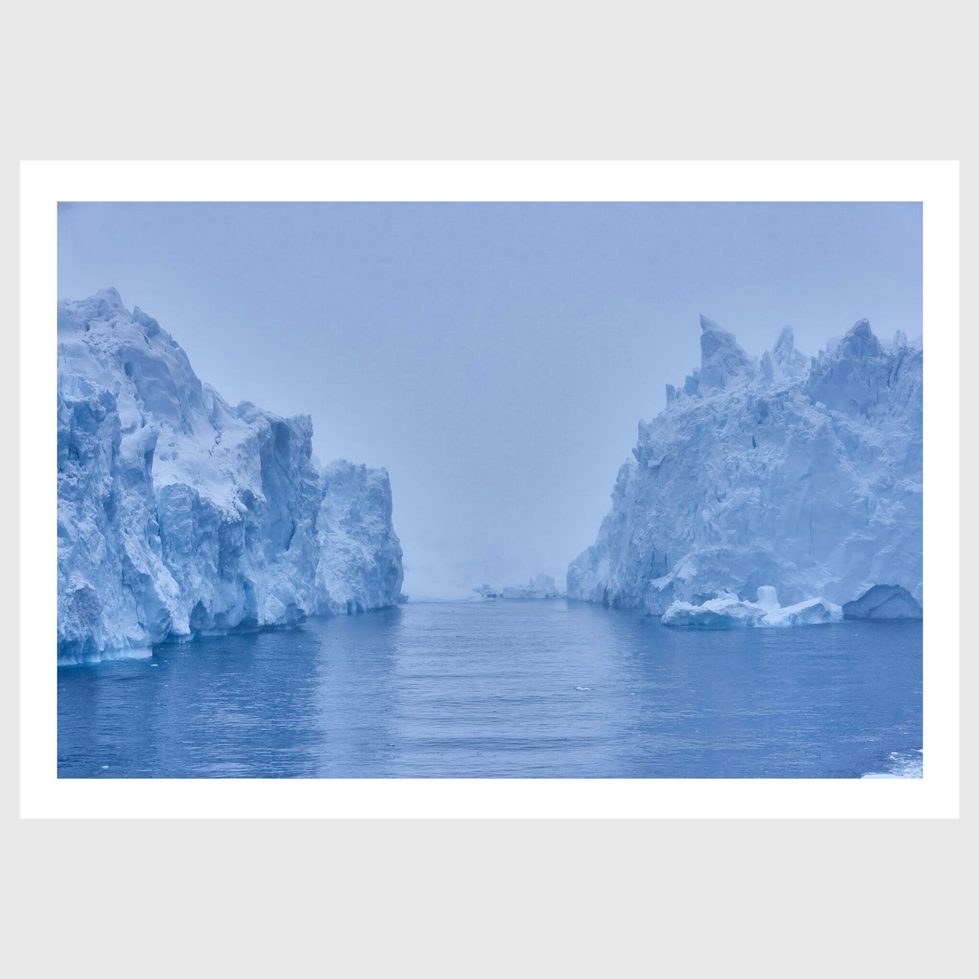 Colour photograph of a large iceberg rising from dark water beneath an overcast sky, Greenland