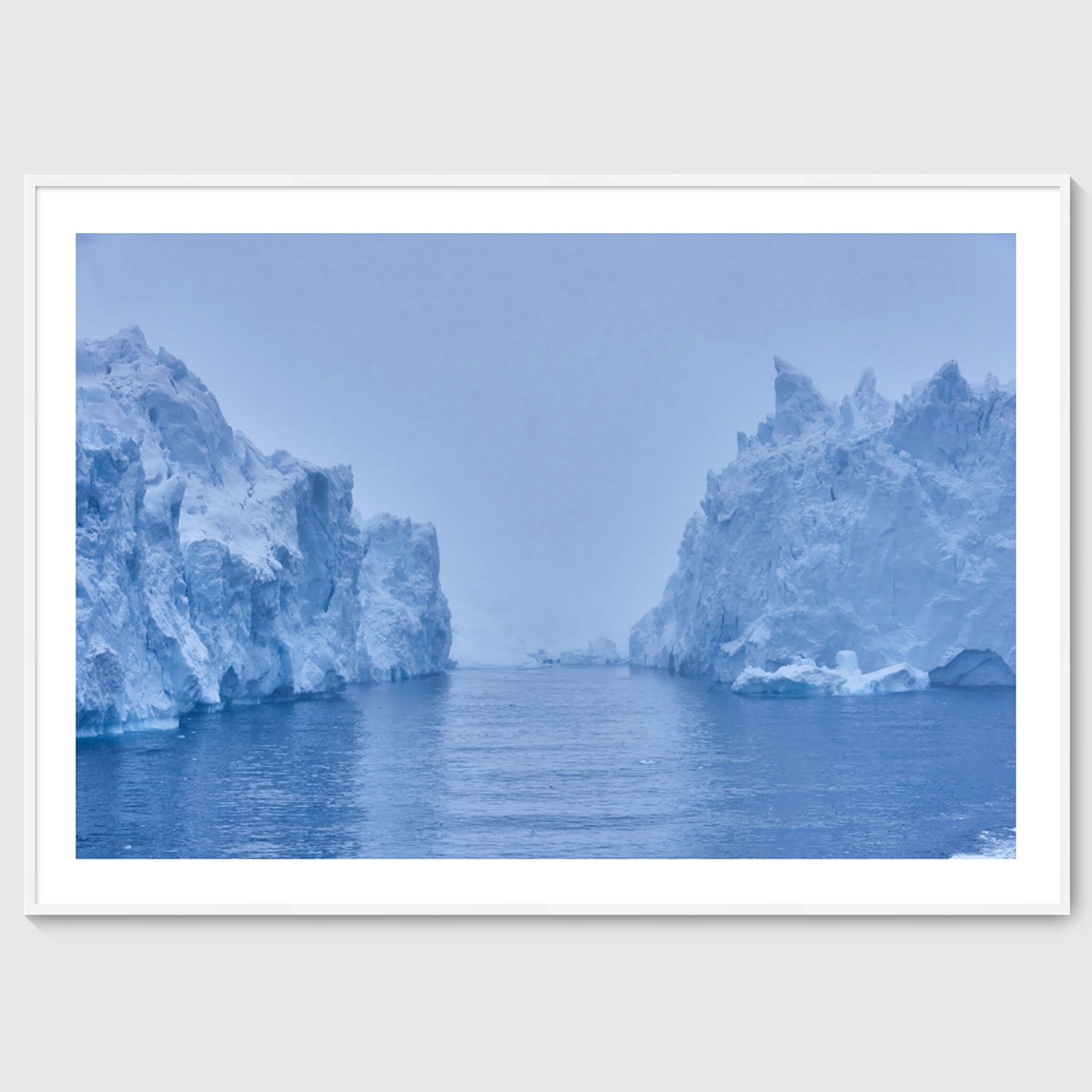 Colour photograph of a large iceberg rising from dark water beneath an overcast sky, shown in a white frame, Greenland