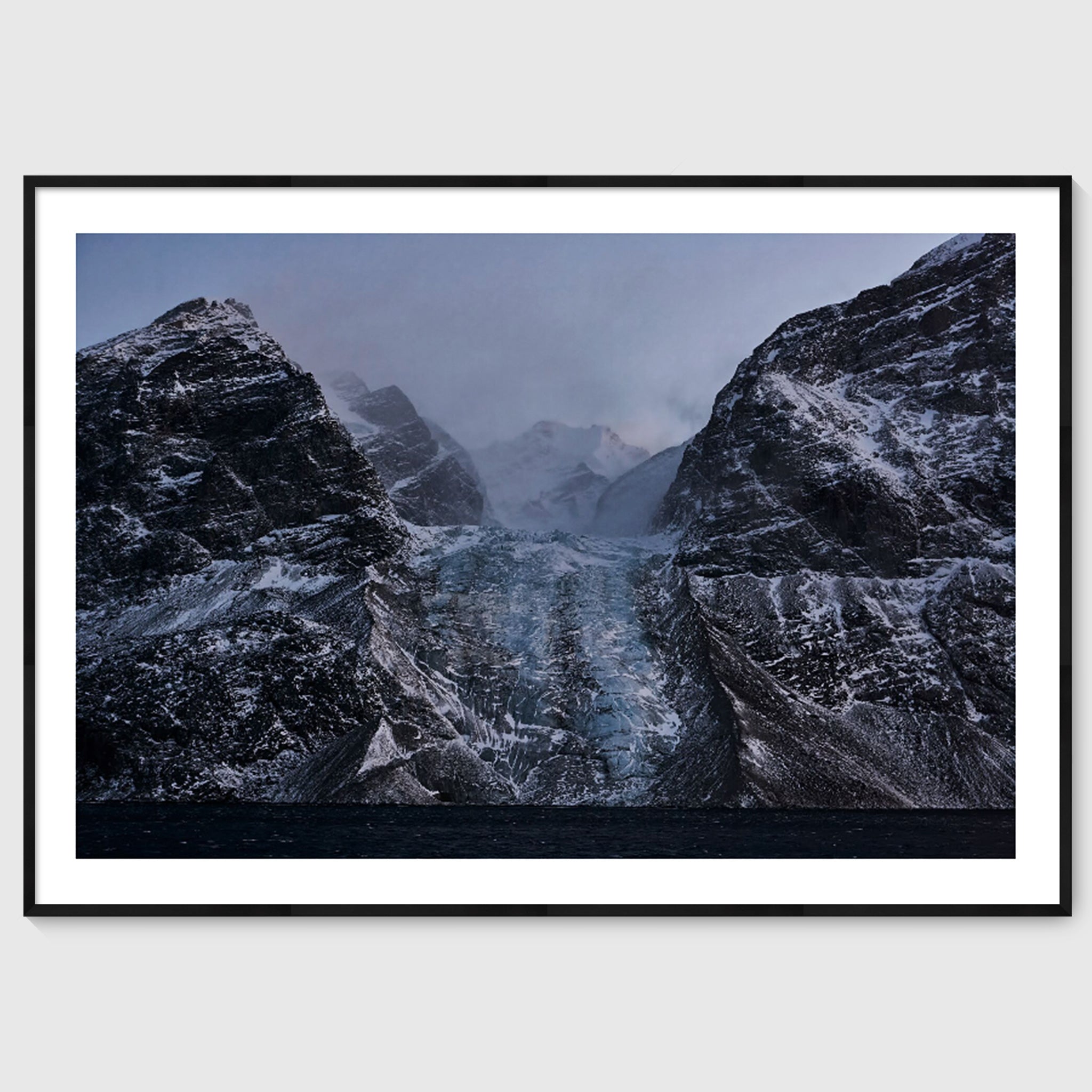 Colour photograph of a glacier descending between dark rock faces, shown in a black frame, Greenland