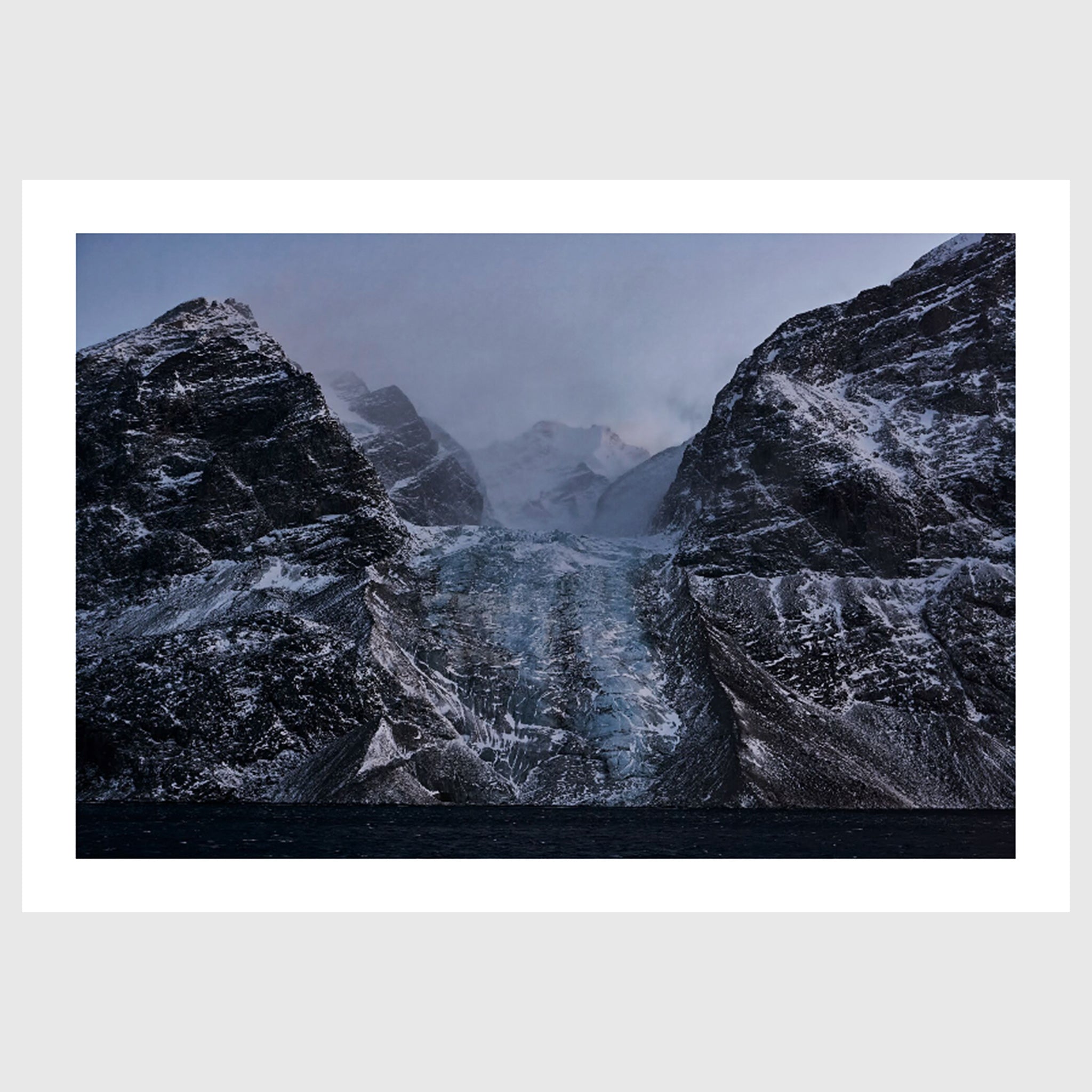 Colour photograph of a glacier descending between dark rock faces, Greenland