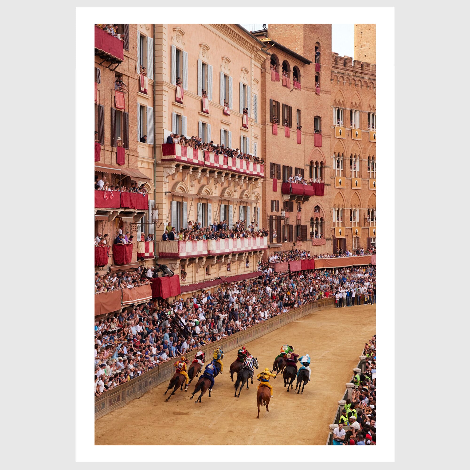 Colour photograph of Piazza del Campo filled with spectators as horses race past historic buildings during the Palio di Siena, sold as an unframed fine art print