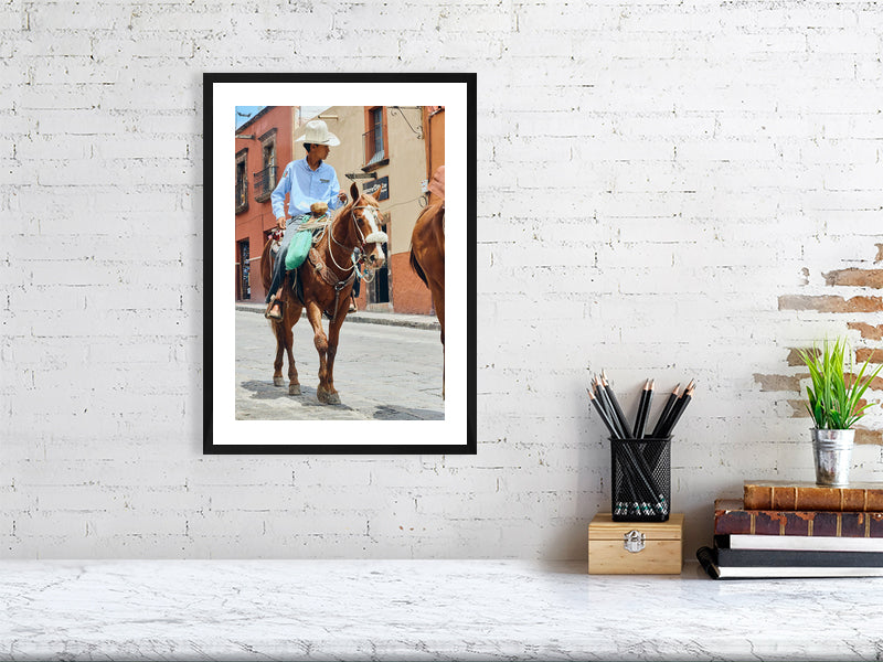 Colour photograph of a vaquero on horseback displayed as a small framed print in a styled interior desktop setting (mockup)