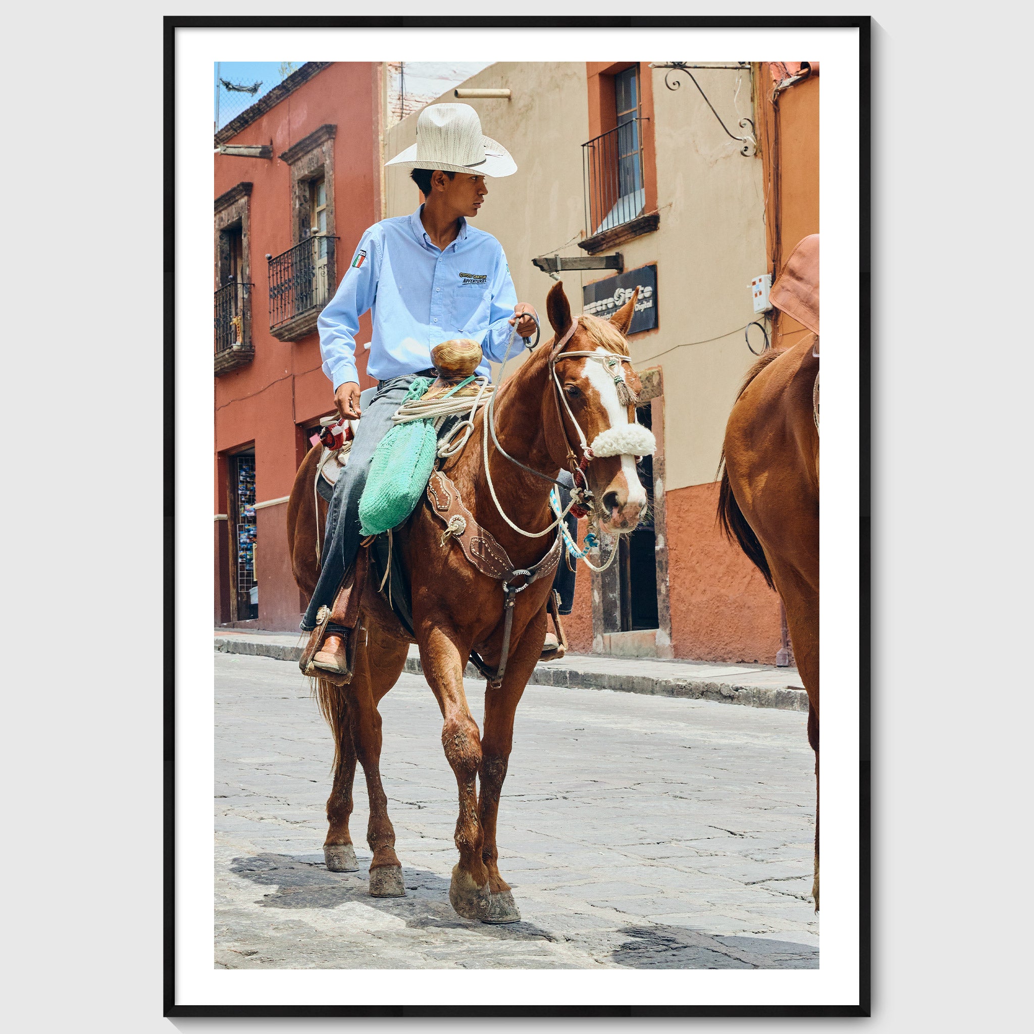Colour photograph of a young vaquero riding a horse through the streets of San Miguel de Allende, shown in a black wooden frame