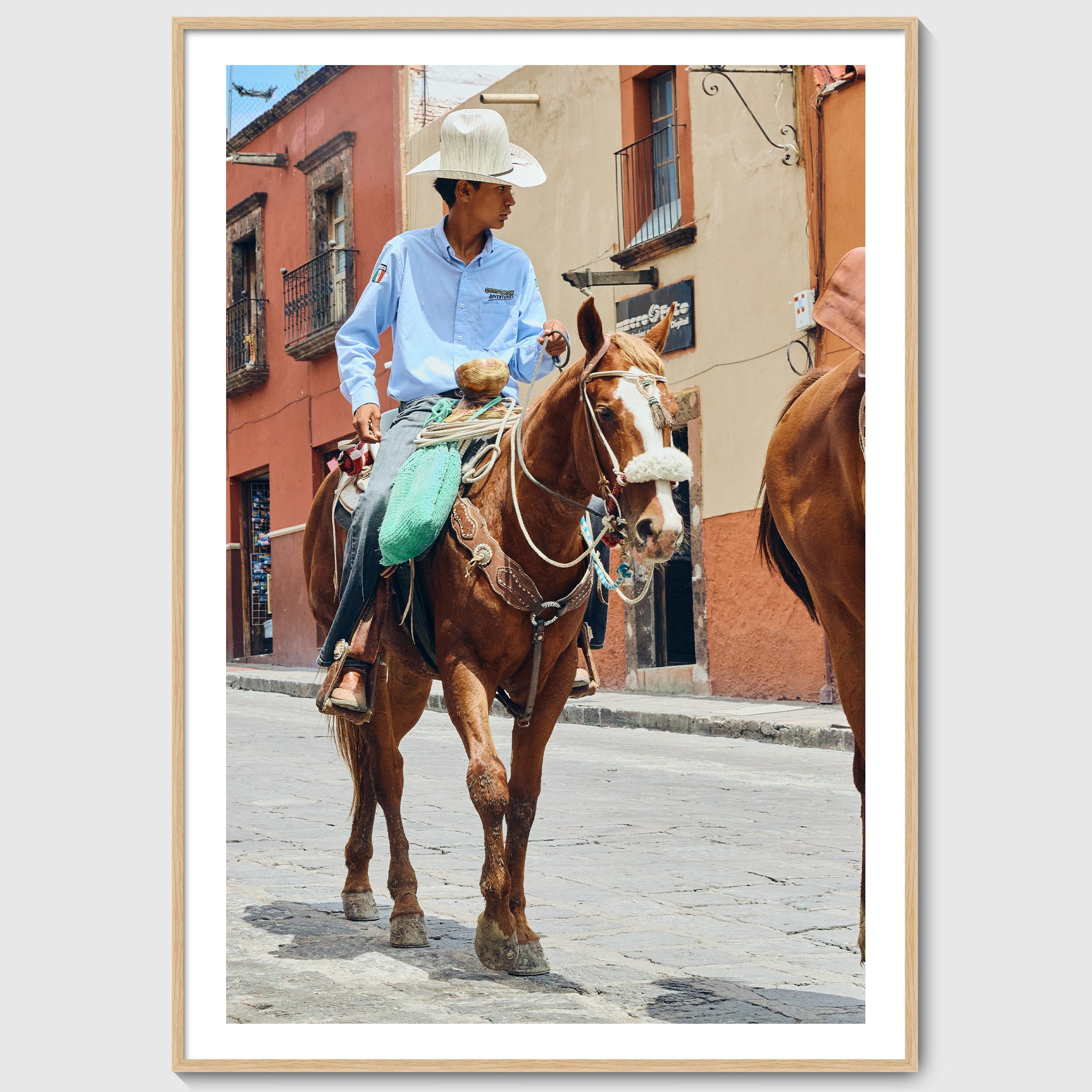 Colour photograph of a young vaquero riding a horse through the streets of San Miguel de Allende, shown in an oak wooden frame