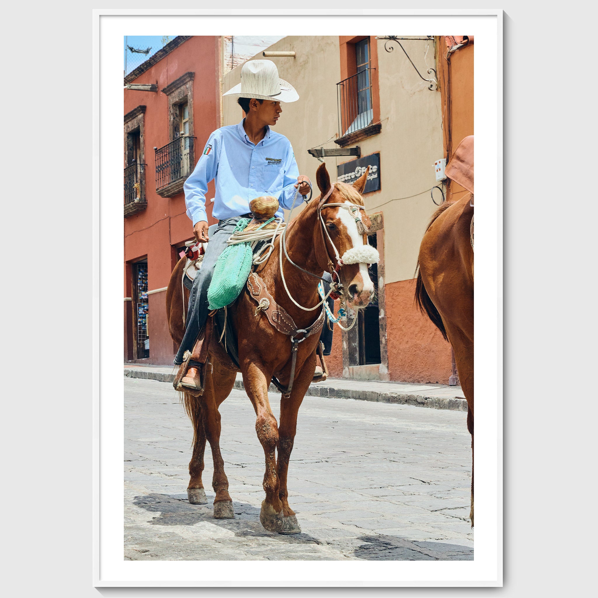 Colour photograph of a young vaquero riding a horse through the streets of San Miguel de Allende, shown in a white wooden frame