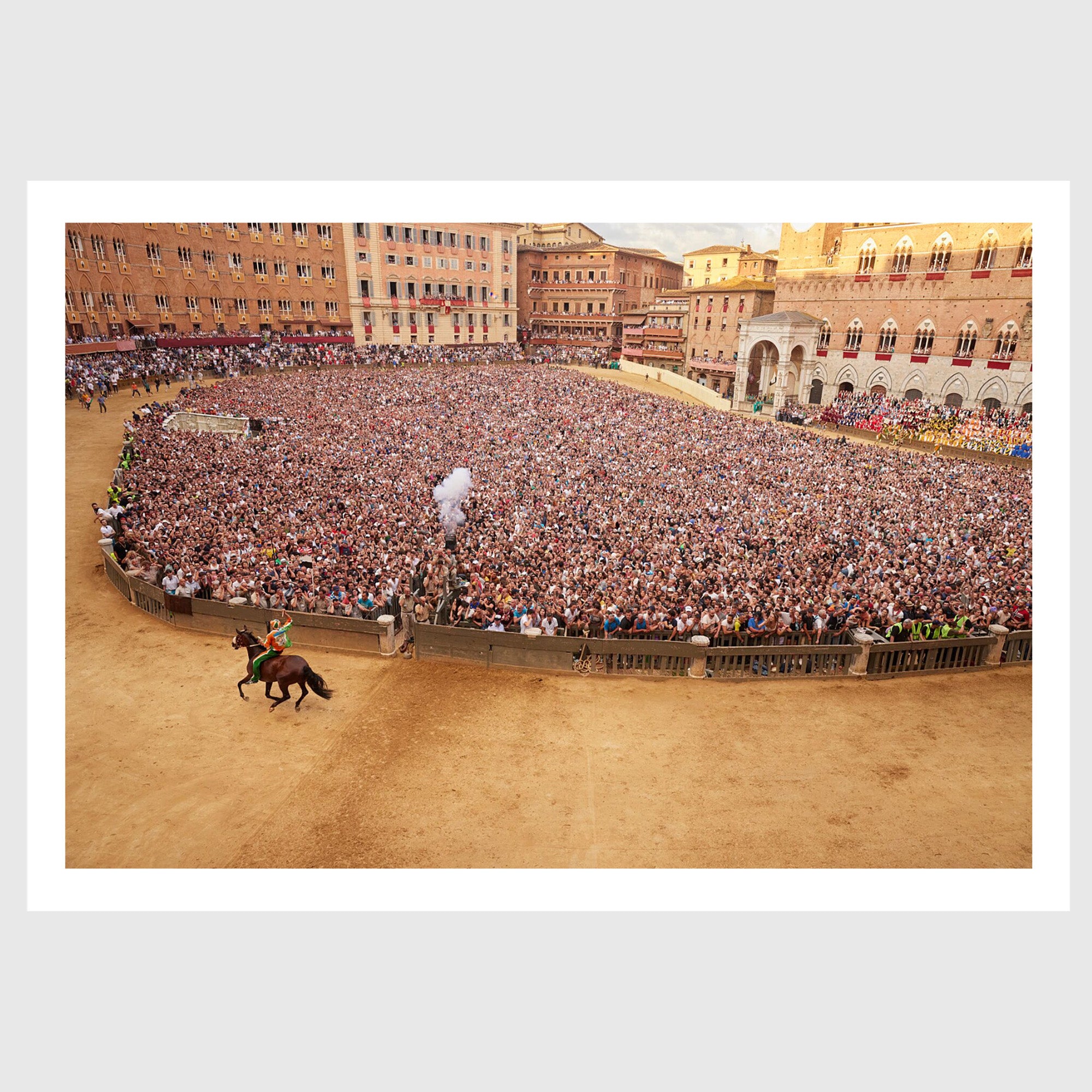 Colour photograph of a jockey on horseback riding past a dense crowd in Piazza del Campo during the Palio di Siena, sold as an unframed fine art print